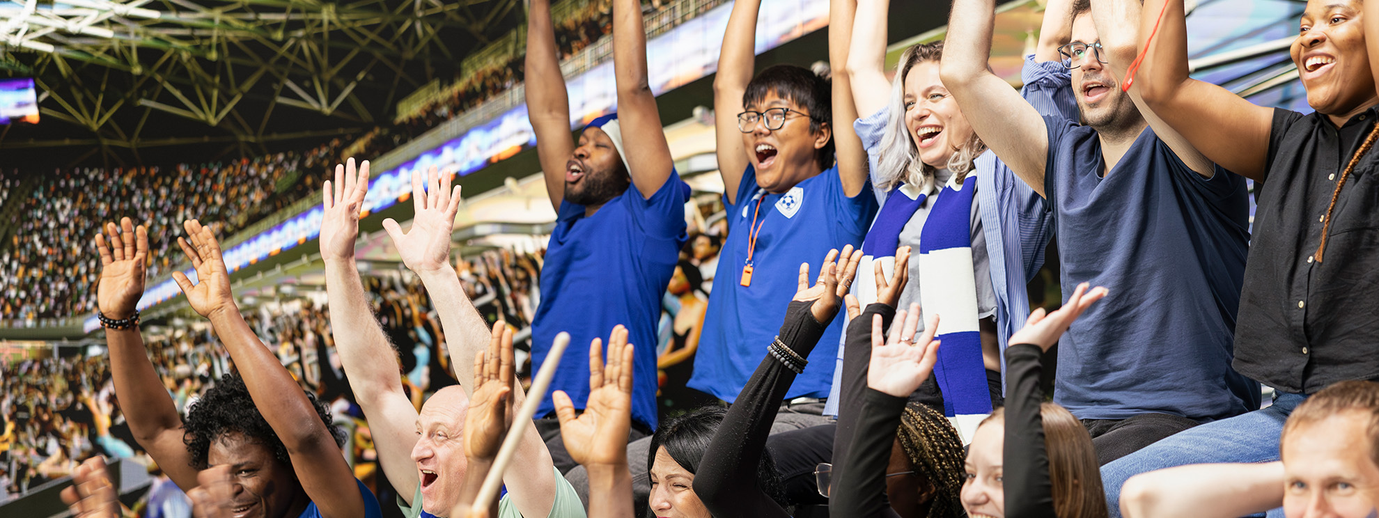 Football fans cheering with arms raised in a packed stadium