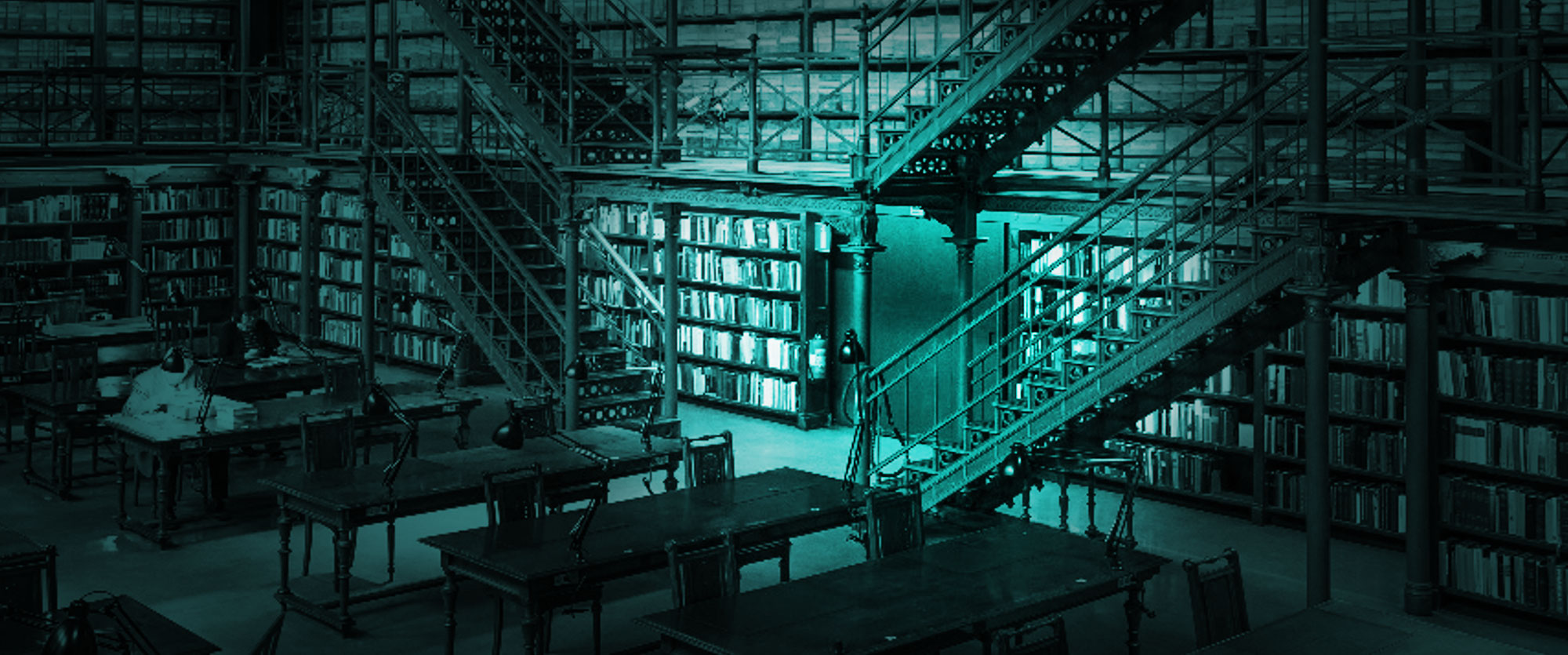 Multi-level library with tall bookshelves, study tables and desk lamps lit by a cool glow from a central opening