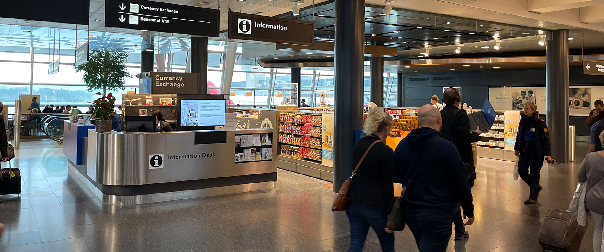 Travelers passing the curved Information Desk in the Zurich Airport terminal